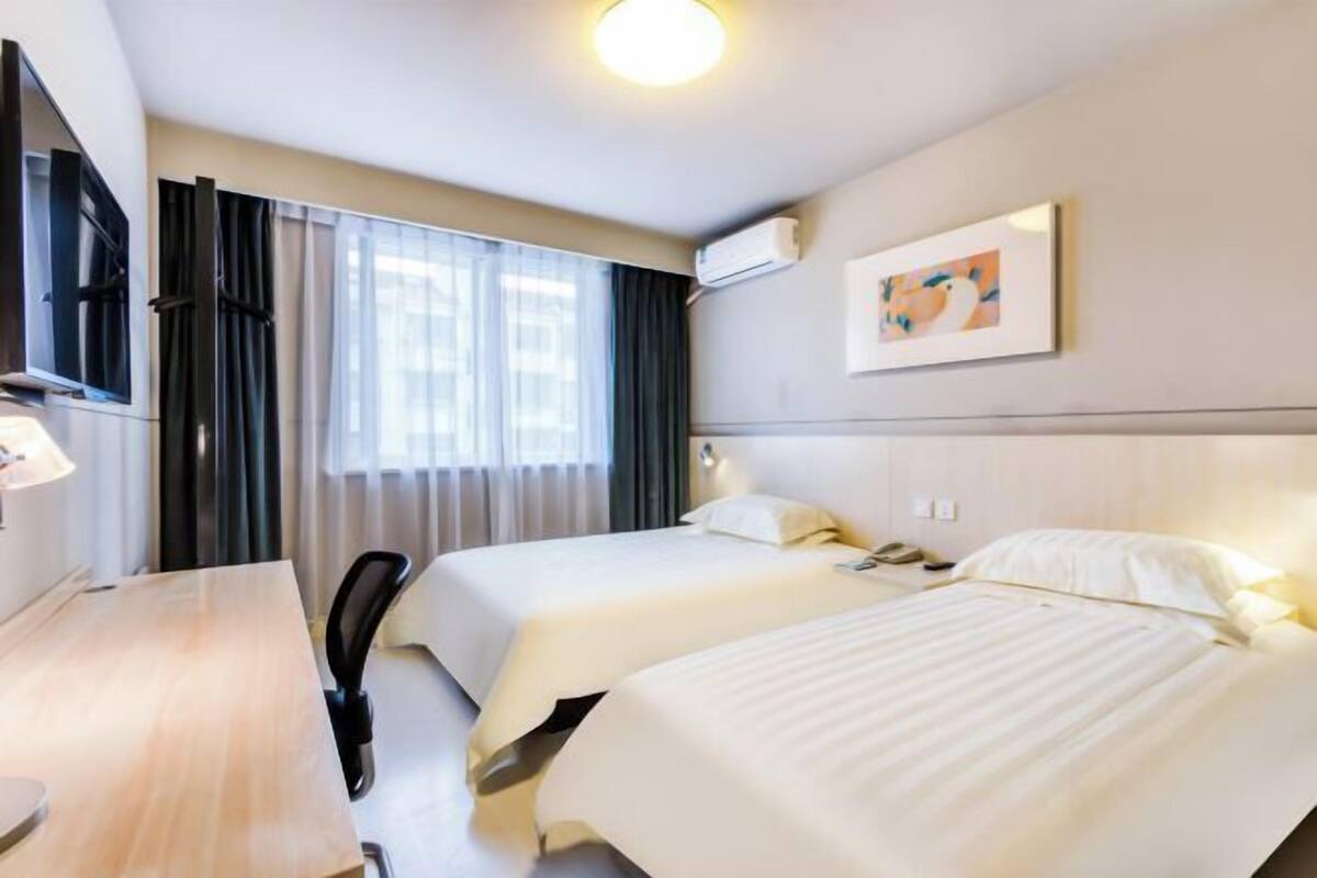 A hotel room with two beds, a desk, a chair, a TV, and a window with curtains.
