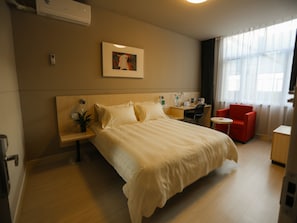 A hotel room with a large bed, a desk, a chair, a small table, and a window with curtains. - Jinjiang Inn (Xinchang Gushan Road Giant Buddhist Temple) (Shaoxing)