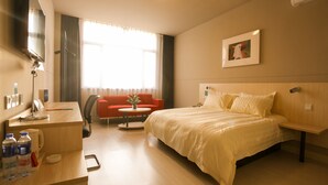 Hotellihuone, jossa on sänky, työpöytä, tuoli, televisio ja ikkuna, jossa on verhot.