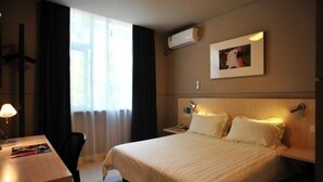 A hotel room with a large bed, a desk, a chair, a nightstand, a lamp, a picture on the wall, and an air conditioning unit. - Jinjiang Inn (Xinchang Gushan Road Giant Buddhist Temple) (Shaoxing)