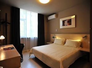 A hotel room with a large bed, a desk, a chair, a nightstand, a lamp, a picture on the wall, and an air conditioning unit. - Jinjiang Inn (Xinchang Gushan Road Giant Buddhist Temple) (Shaoxing)
