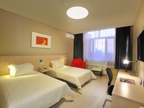 A hotel room with two beds, a desk, a chair, a desk lamp, a window with curtains, and a wall-mounted air conditioner. - Jinjiang Inn Daqing Lande Lake (Daqing)