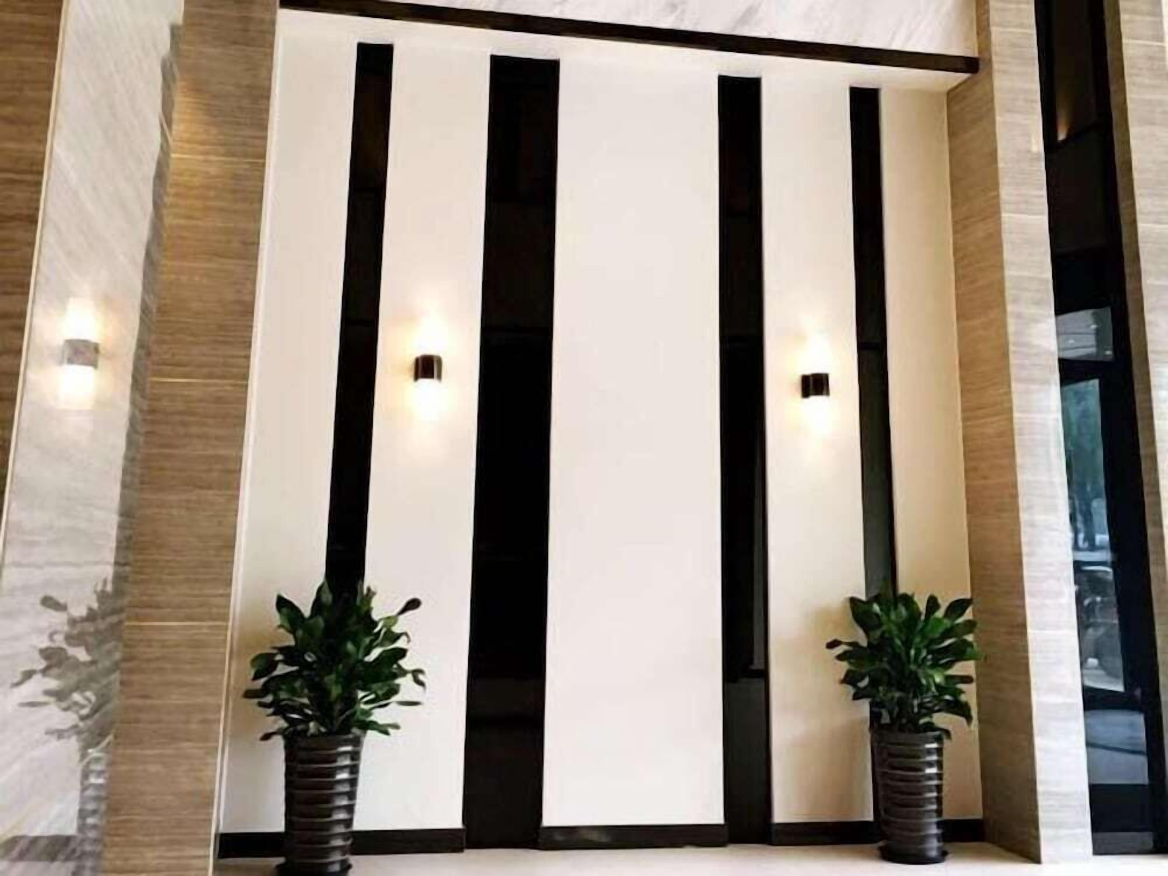 Un interior moderno con un separador blanco y líneas verticales negras, flanqueado por dos plantas en macetas.