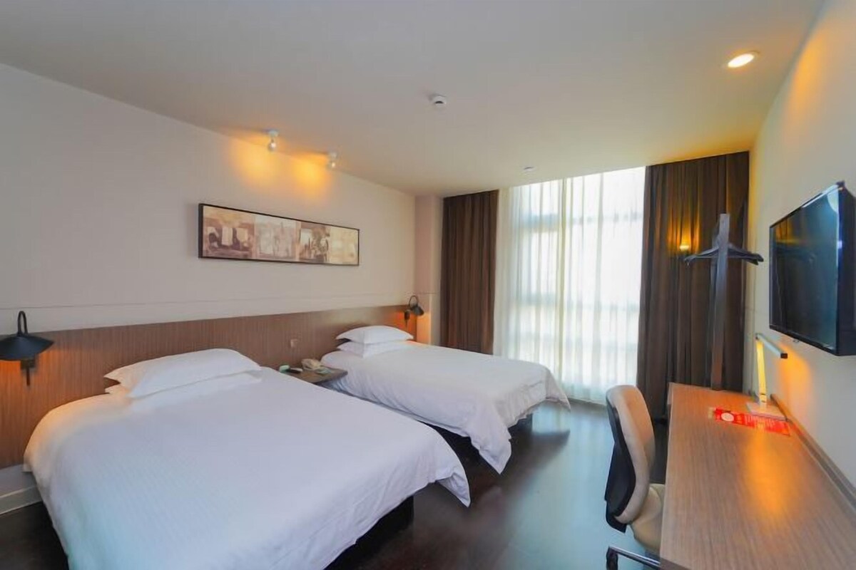 Une chambre d’hôtel avec deux lits, un bureau, une télévision et une fenêtre avec des rideaux.