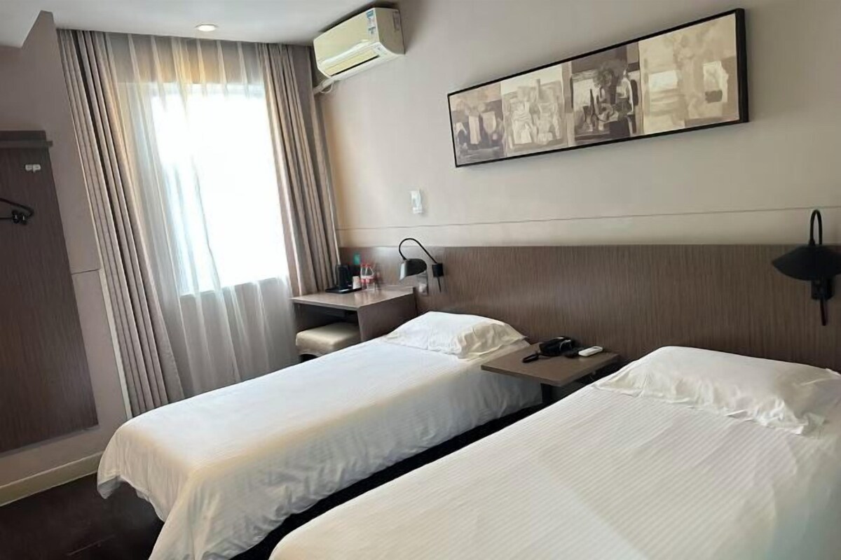 Habitació d'hotel amb dos llits, un escriptori, una cadira, un aire condicionat fixat a la paret i un quadre.