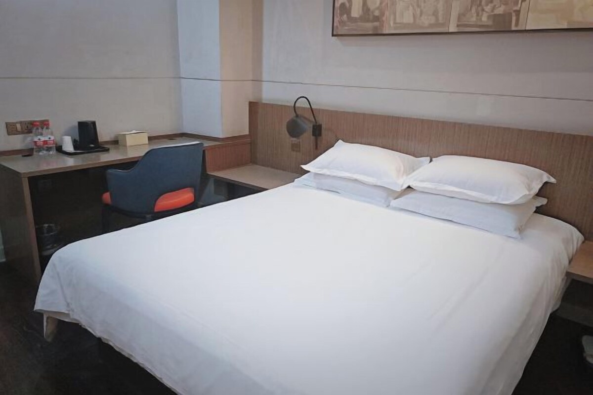 A hotel room with a bed, a desk, a chair, and a wall-mounted lamp.