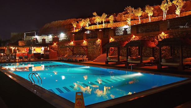A nighttime swimming pool with lounge chairs and a stone wall backdrop. - Naama Blue hotel (Sharm El Sheikh)