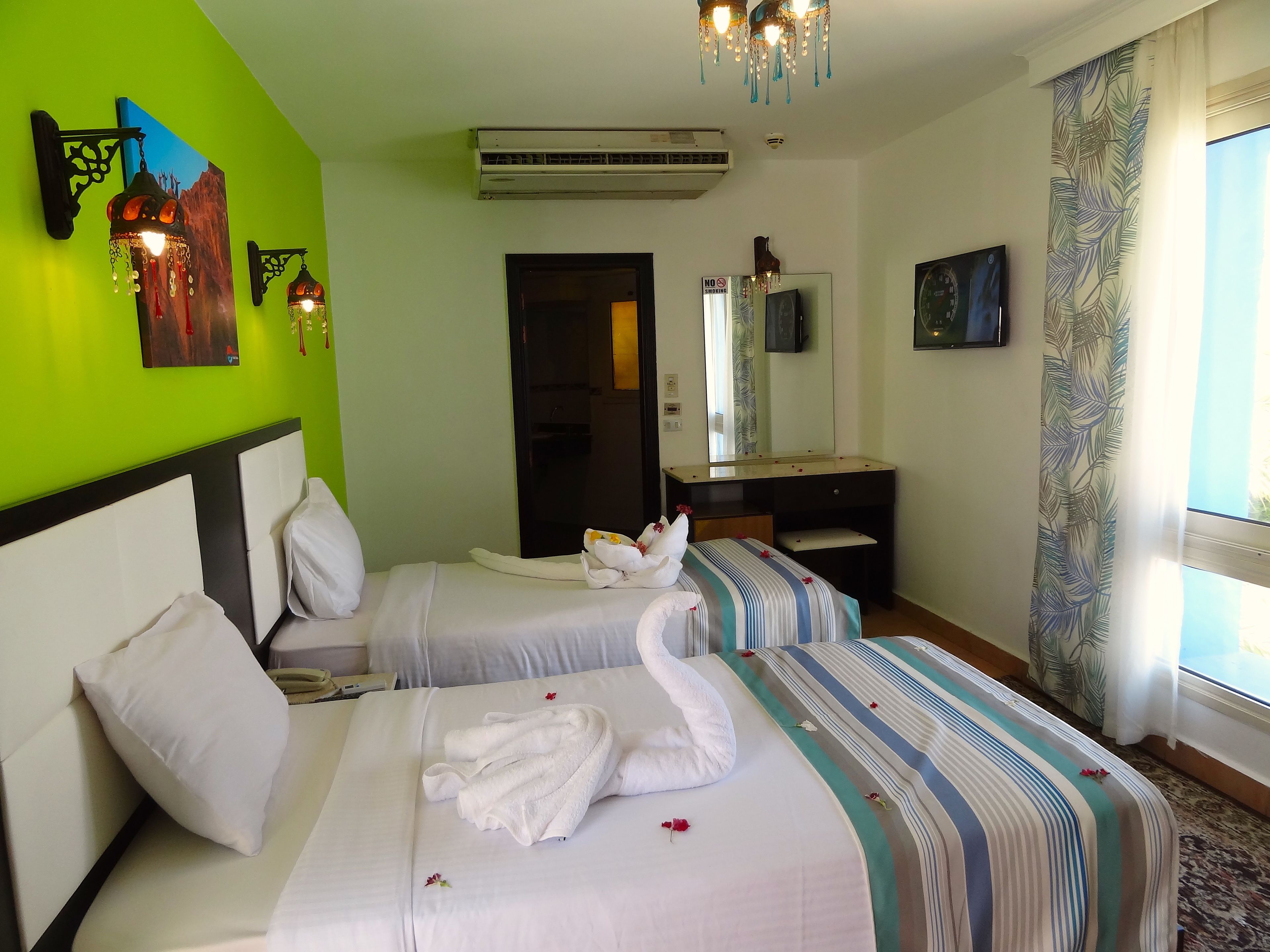 A hotel room with two beds, a desk, a mirror, and a television.