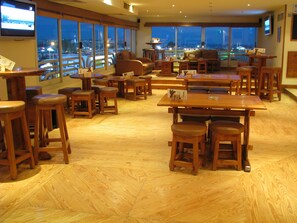 Un restaurant doté de meubles en bois, de grandes fenêtres et offrant une vue sur la ville la nuit.