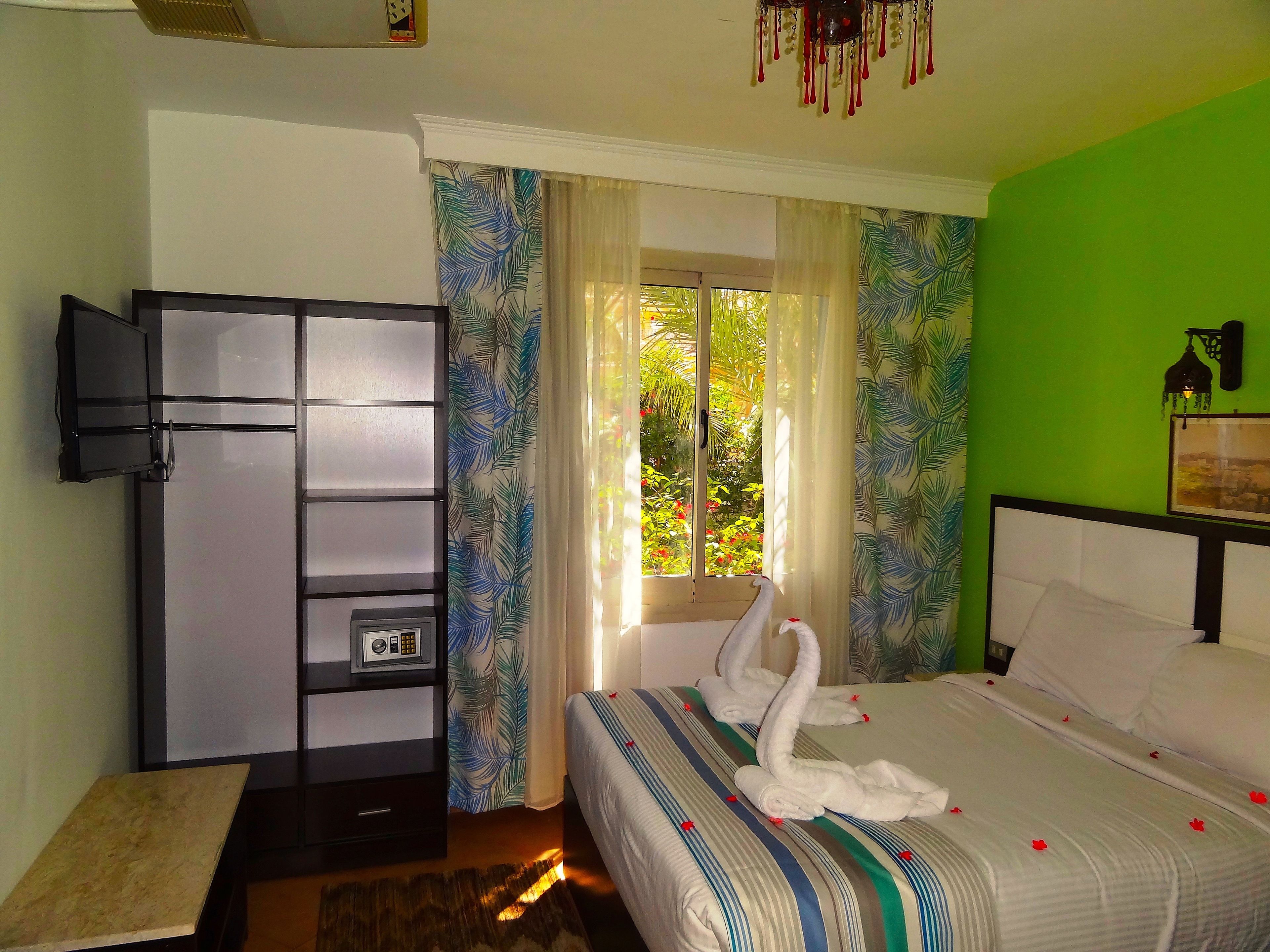 Une chambre d’hôtel avec un lit, une télévision, une armoire et une fenêtre avec des rideaux.