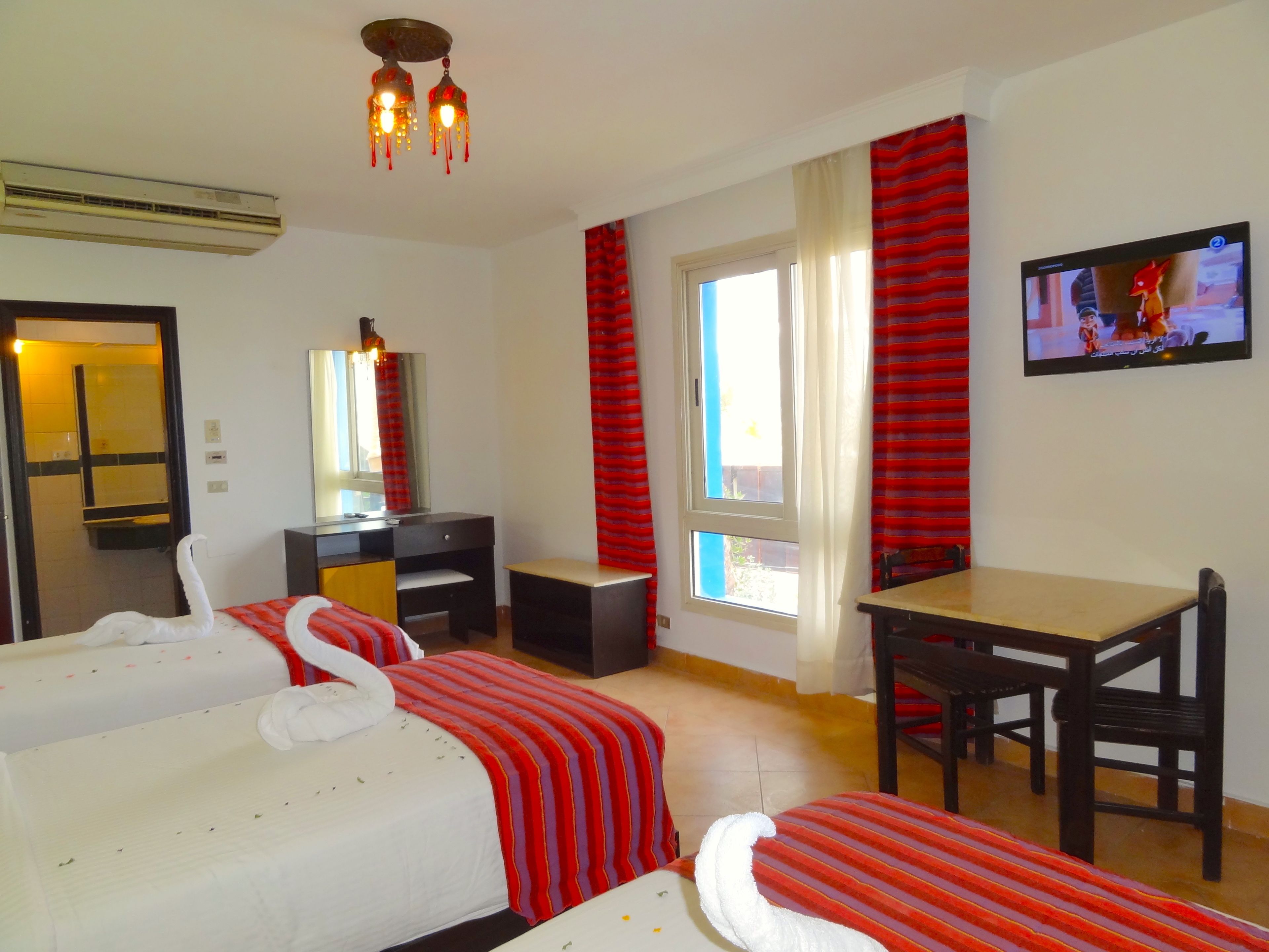 Une chambre d’hôtel avec deux lits, un bureau, une chaise, une télévision et une fenêtre avec des rideaux.