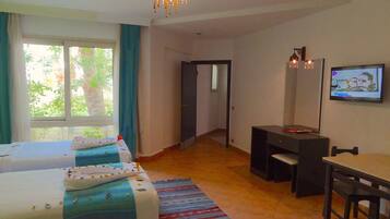 Une chambre d’hôtel avec deux lits, un bureau, une chaise, une télévision et une vue sur la verdure environnante.