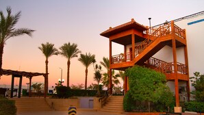 A wooden structure with a balcony and stairs, surrounded by palm trees and a tiled patio area. - Naama Blue hotel (Sharm El Sheikh)