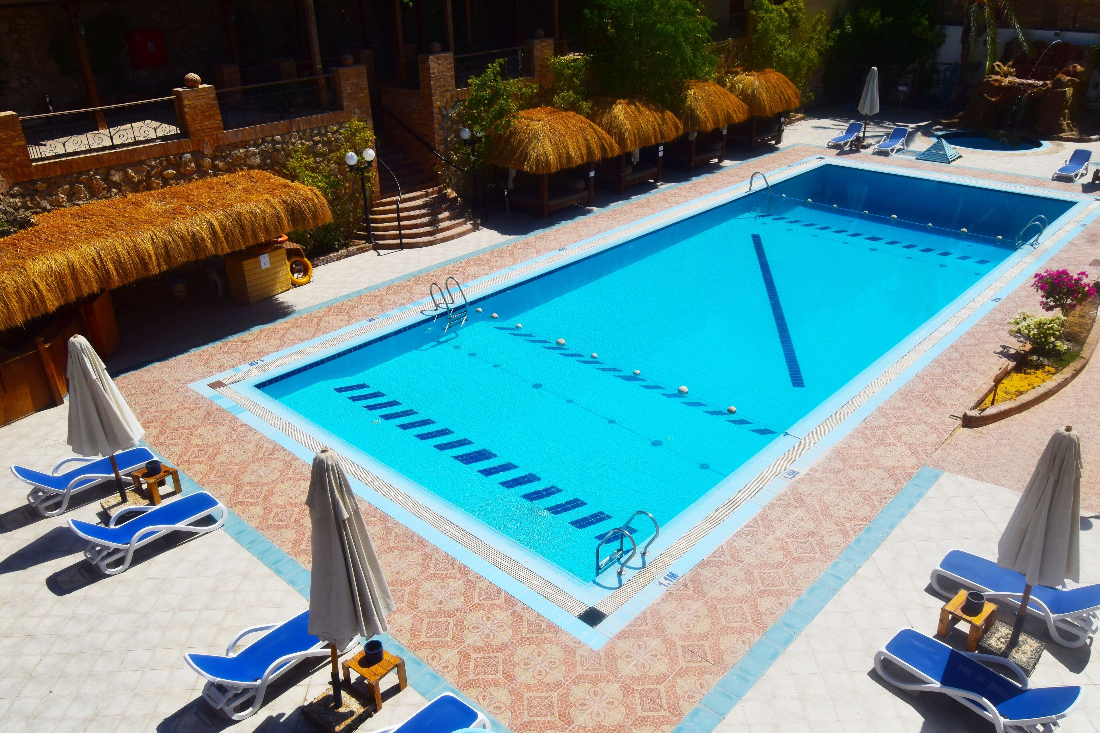 Una piscina con agua azul, rodeada de sillas de descanso y sombrillas.