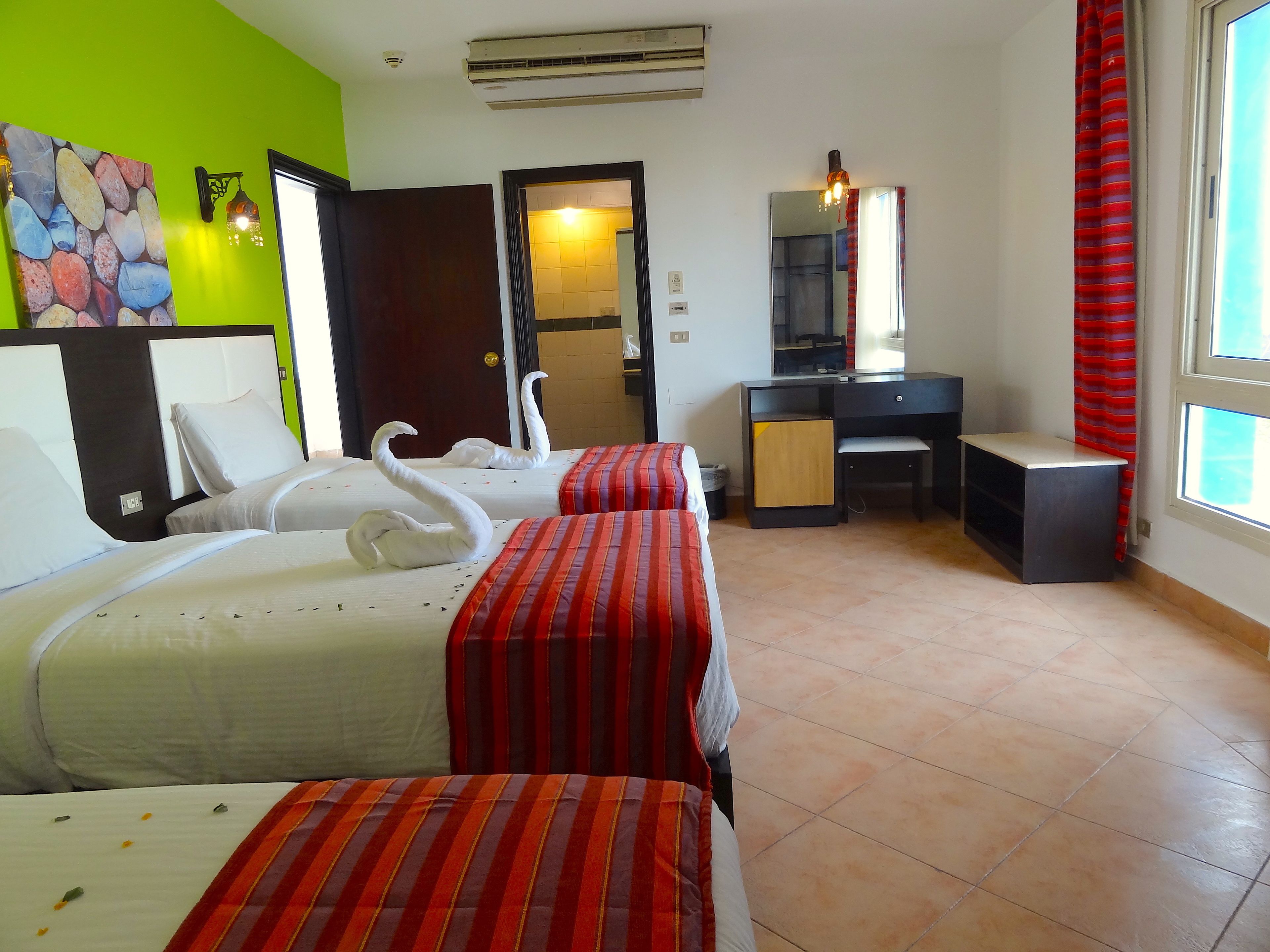 A hotel room with two beds, a desk, a chair, a mirror, and a window with curtains.