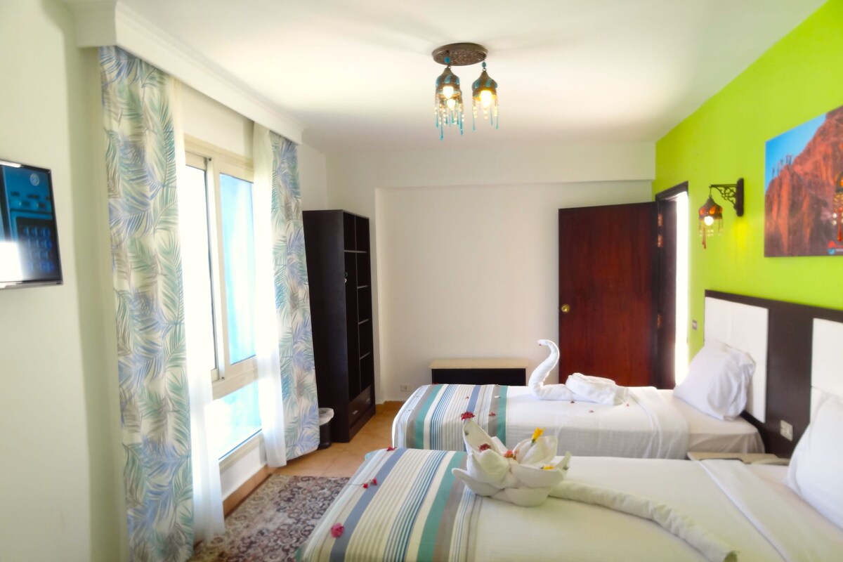 Habitación de hotel con dos camas, un armario, un cuadro y una ventana con cortinas.