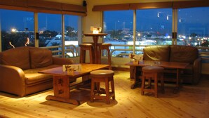 A cozy living room with a brown leather sofa, wooden coffee table, and a small stool. Large windows offer a view of the city at night. - Naama Blue hotel (Sharm El Sheikh)