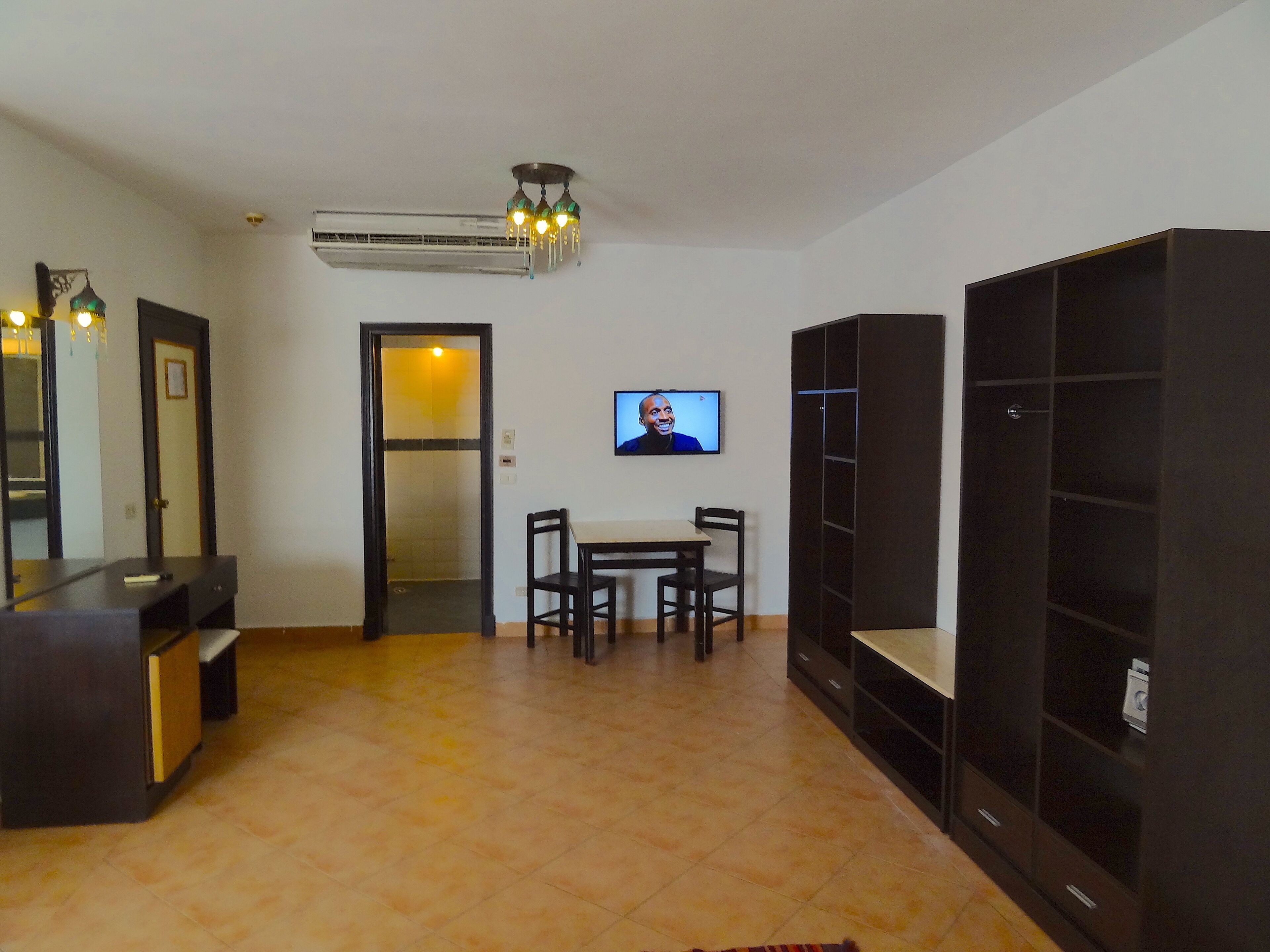 A living room with a TV, a dining table, chairs, a sofa, a TV stand, and a bookshelf.