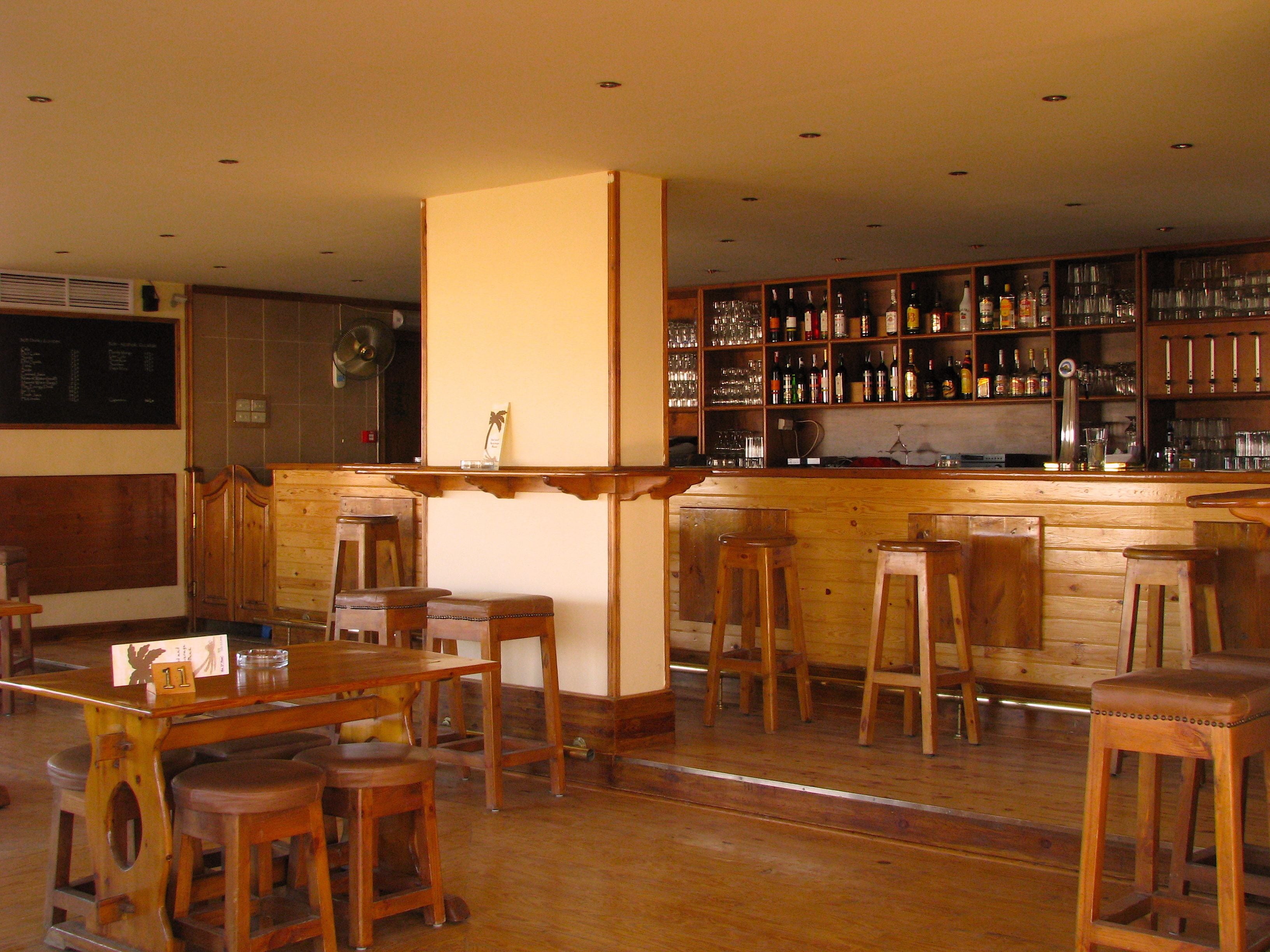 A bar area with wooden stools, a bar counter, and shelves stocked with bottles and glasses.