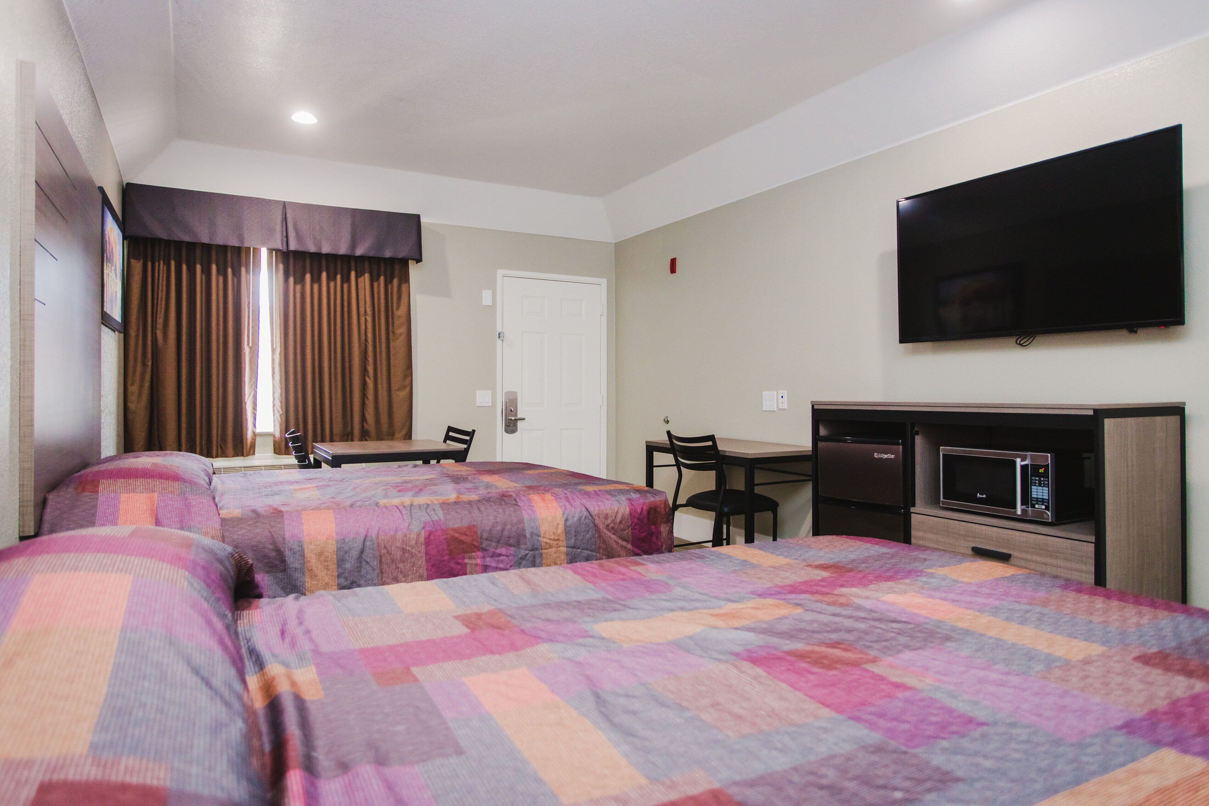 A hotel room with two beds, a desk, a chair, a television, and a microwave.