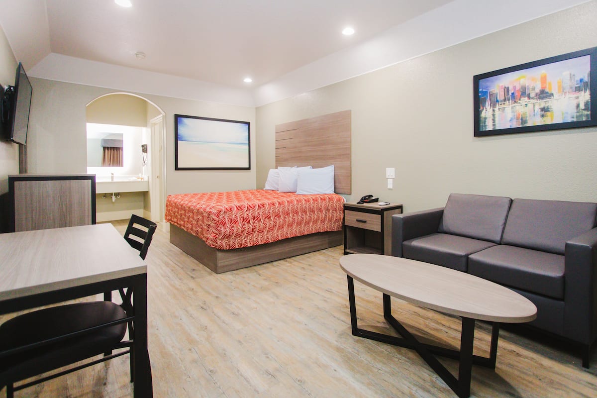 A hotel room with a bed, a sofa, a dining table, and a TV.