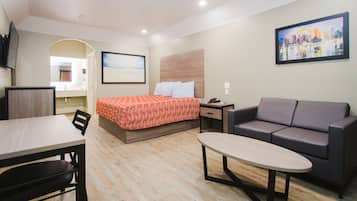 A hotel room with a bed, a sofa, a dining table, and a TV.
