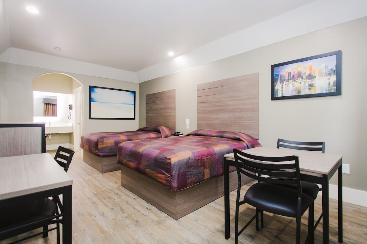 A hotel room with a bed, a desk, and a chair. There is a painting on the wall and a window with curtains.