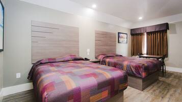 A hotel room with two beds, a wooden headboard, a dining table, and a window with curtains.