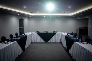 Un salón de conferencias con una larga mesa, sillas, botellas de agua y una pantalla de proyector.