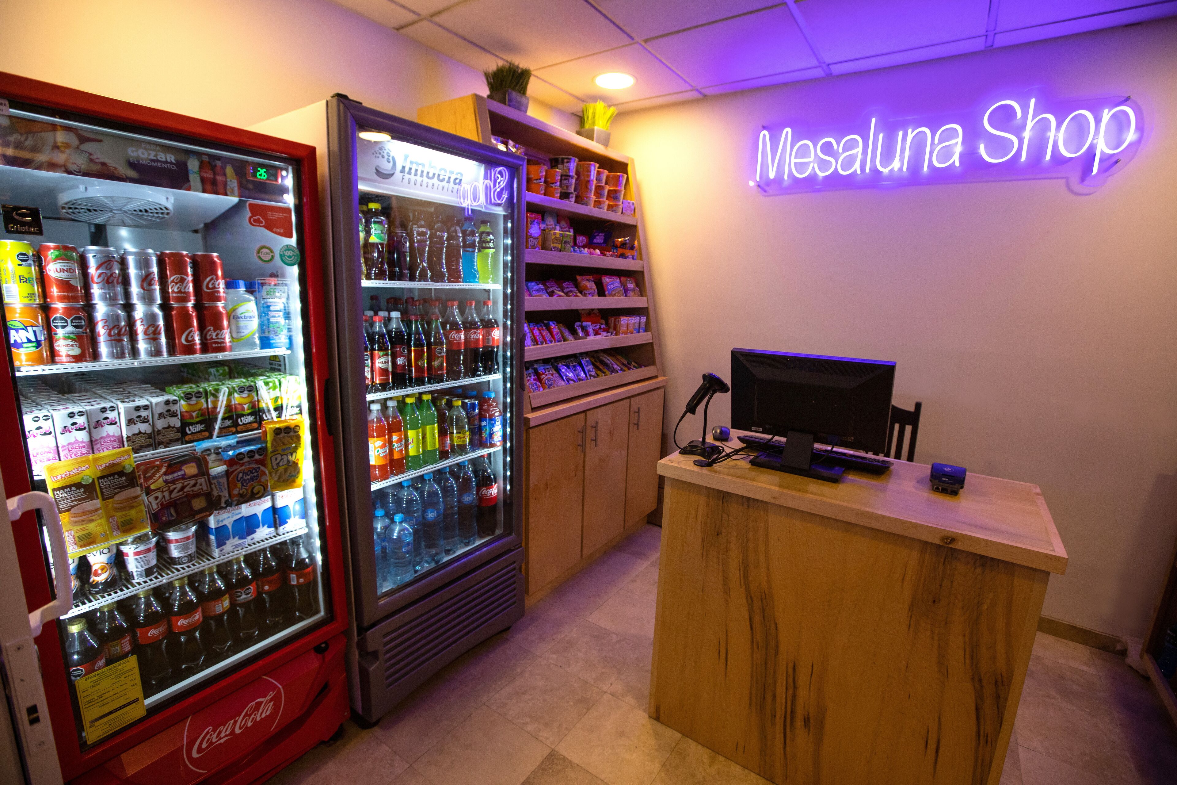 A vending machine area with Coca-Cola and other beverages, a snack shelf, and a reception desk with a computer.