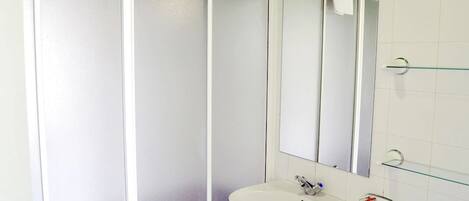 A bathroom with a white sink, a mirror, and a glass shelf.