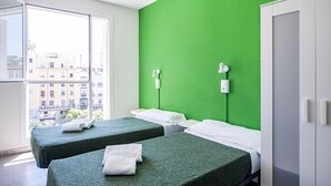 A room with two beds, a green wall, a window with a view of buildings, and a white wardrobe. - El Patio de Chueca - Hostel (Madrid)