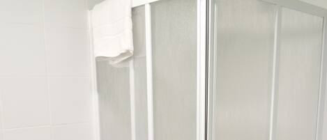 A bathroom with a shower enclosure, a toilet, and a trash bin.