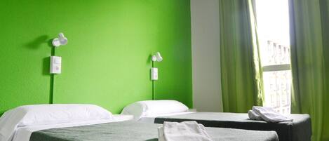 A hotel room with two beds, green walls, a window with green curtains, and a view of buildings outside.