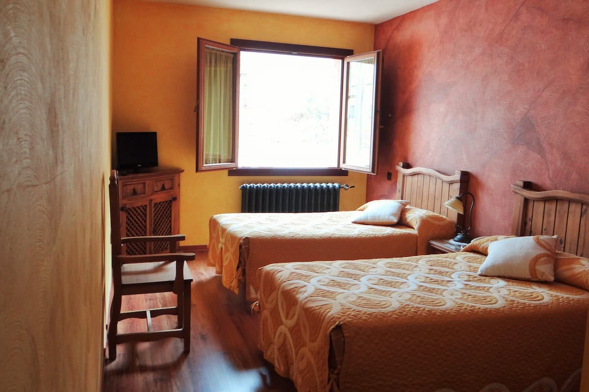 Una habitación con dos camas, un armario de madera y una ventana con cortinas.