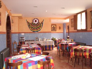 Un comedor con varias mesas cubiertas con manteles coloridos, sillas de madera y un tapiz decorativo.