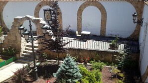 Une cour bordée de murs en pierre, dotée d’un portail en métal et agrémentée de plantes en pot.