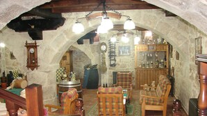 Une pièce rustique aux murs de pierre, meublée de meubles en bois, avec un escalier en bois et un coin bar où sont exposées des bouteilles et des verres.
