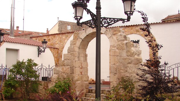 Un espace extérieur agrémenté d’arches en pierre, d’un lampadaire en métal et d’un jardin où poussent différentes espèces de plantes.