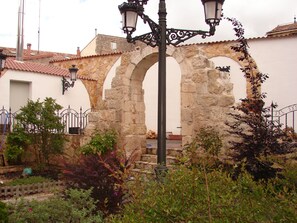 Un espacio al aire libre con arcos de piedra, un farol de metal y un jardín con diversas plantas.