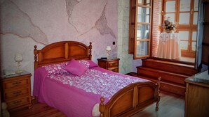 Une chambre avec un lit en bois, un mur décoré d’un motif imitant le marbre, une fenêtre offrant une vue agréable et une table de chevet en bois avec une lampe.