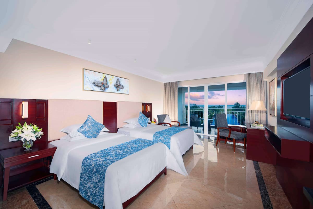 A hotel room with two beds, a TV, a balcony with a view, and a desk with a lamp.