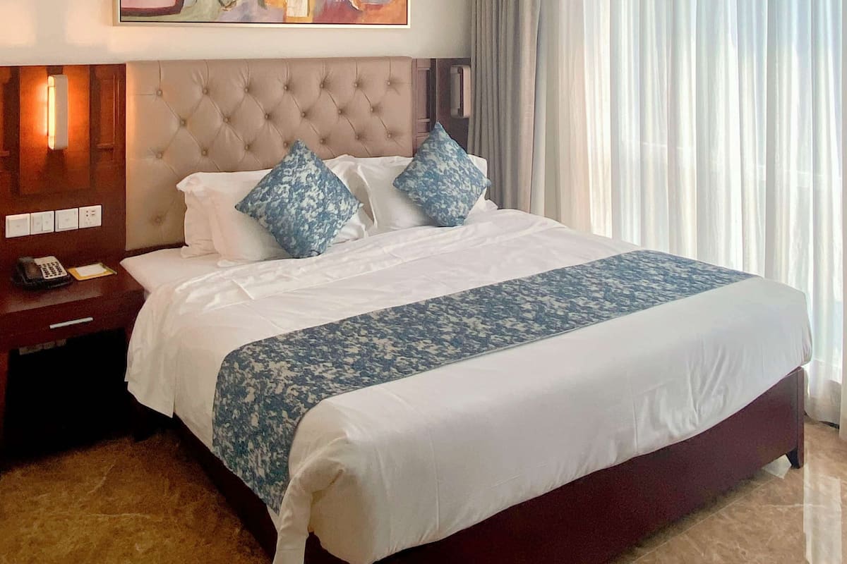 A hotel room with a large bed, a wooden nightstand with a telephone, and a window with curtains.