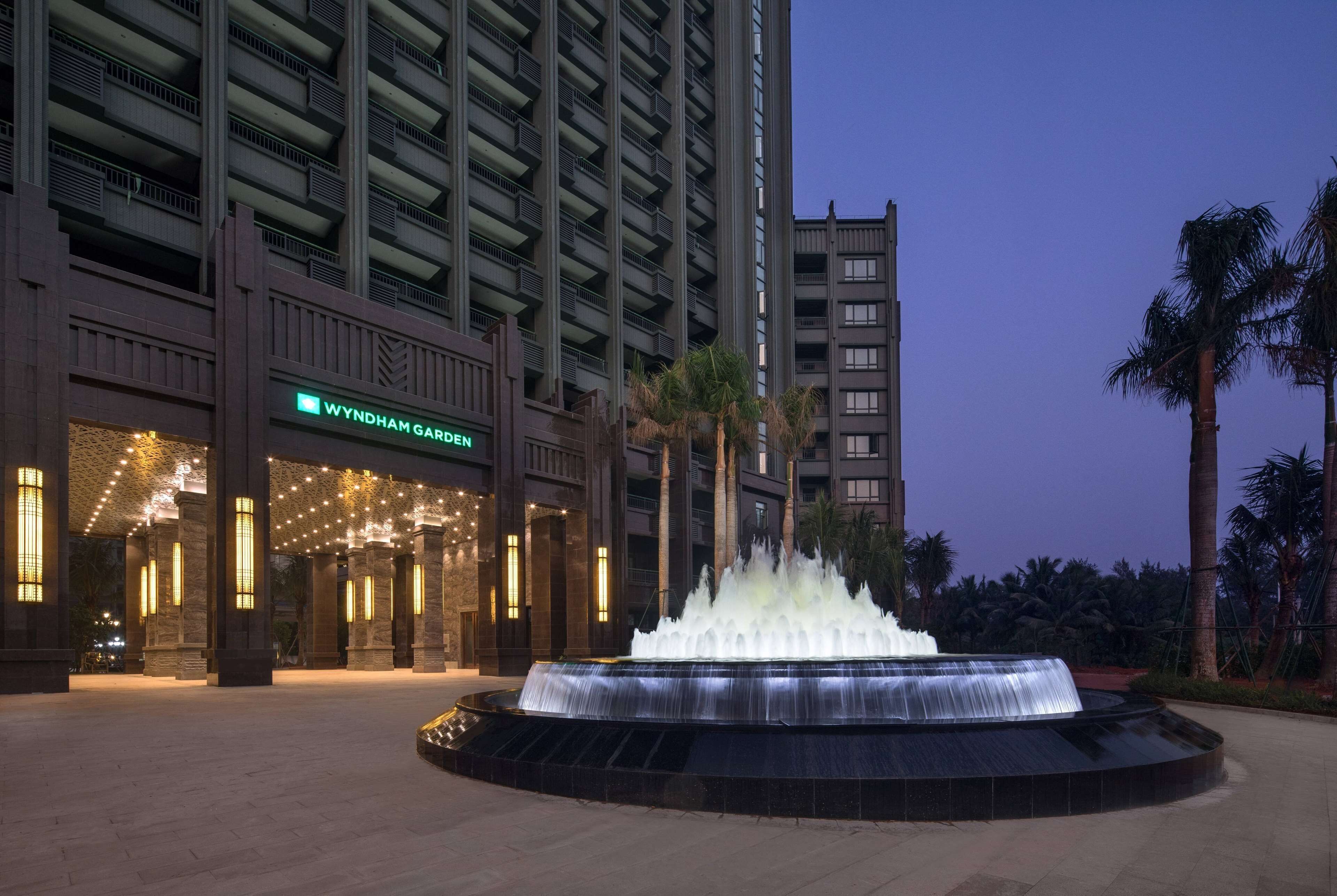 Entrada de un hotel con una fuente de agua, un cartel que dice "Wyndham Garden" y una fachada de edificio moderna.