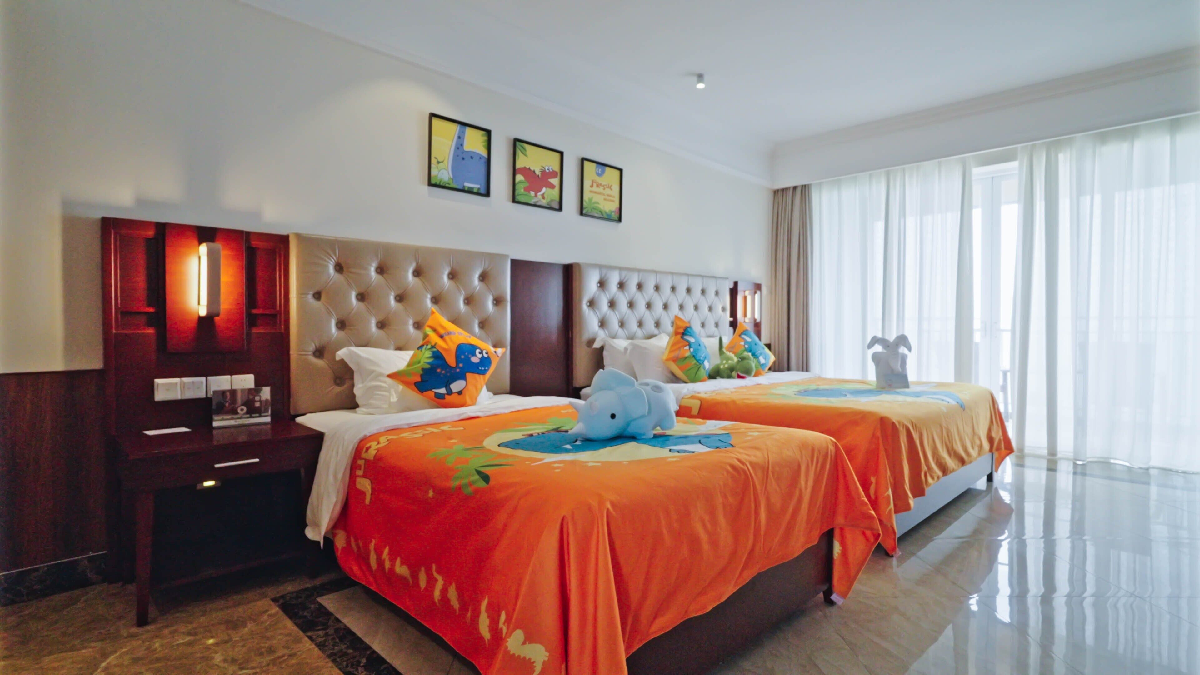 Una habitación de hotel con dos camas, cada una con una colcha naranja y una decoración de elefante de dibujos animados. Hay cuadros enmarcados en la pared sobre las camas.