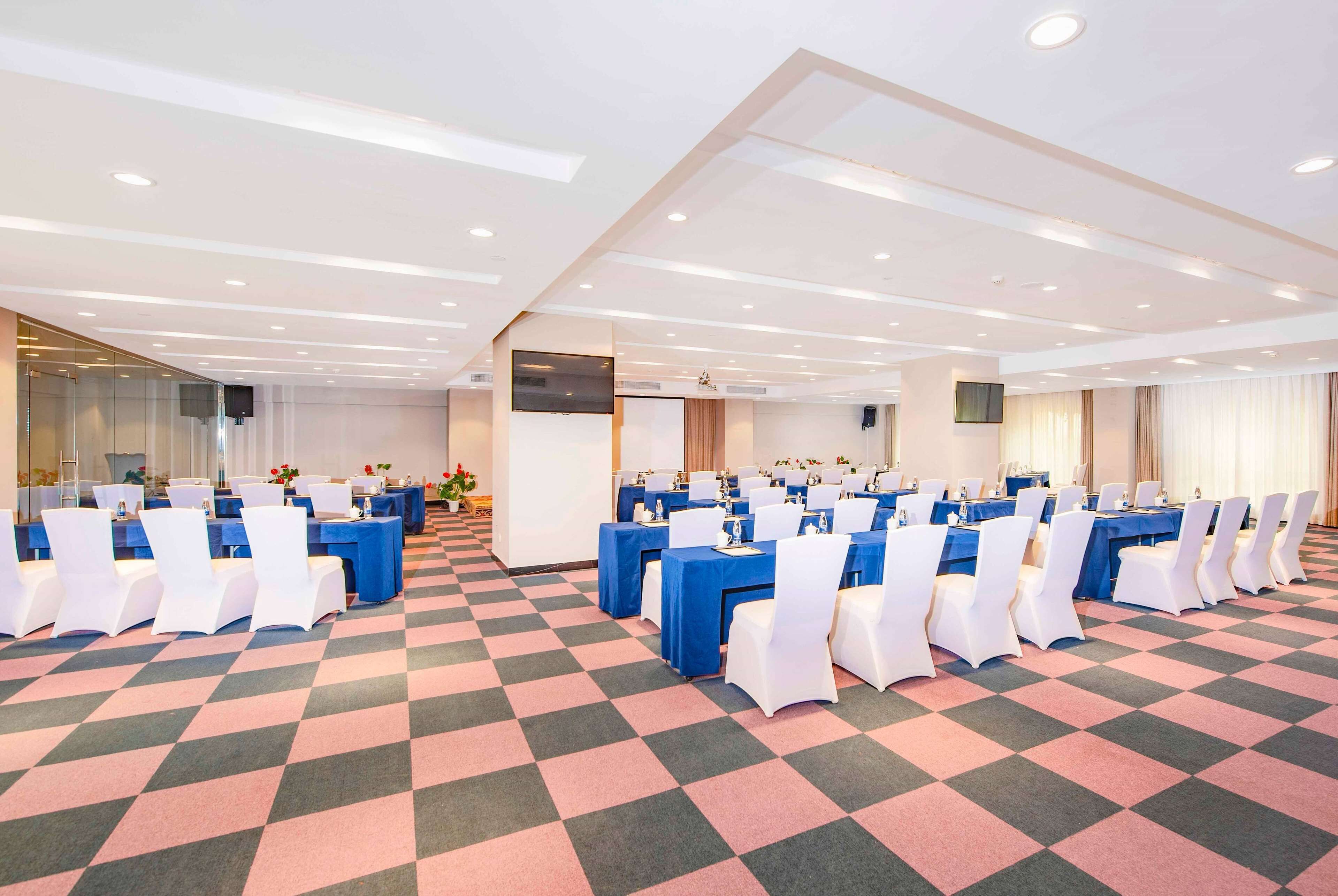 A conference room with multiple tables and chairs, a large screen, and a patterned carpet.