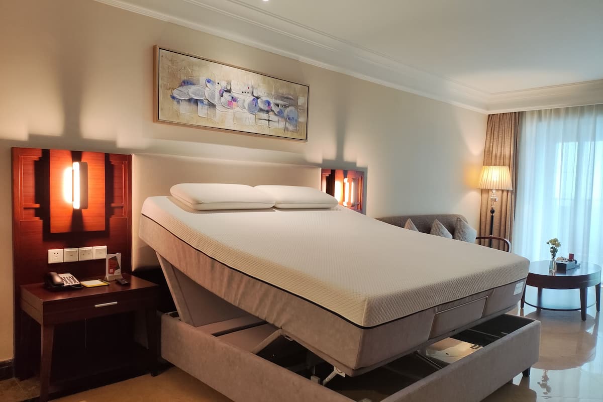 A hotel room with a bed, bedside tables, a lamp, a painting, and a view of the outside.