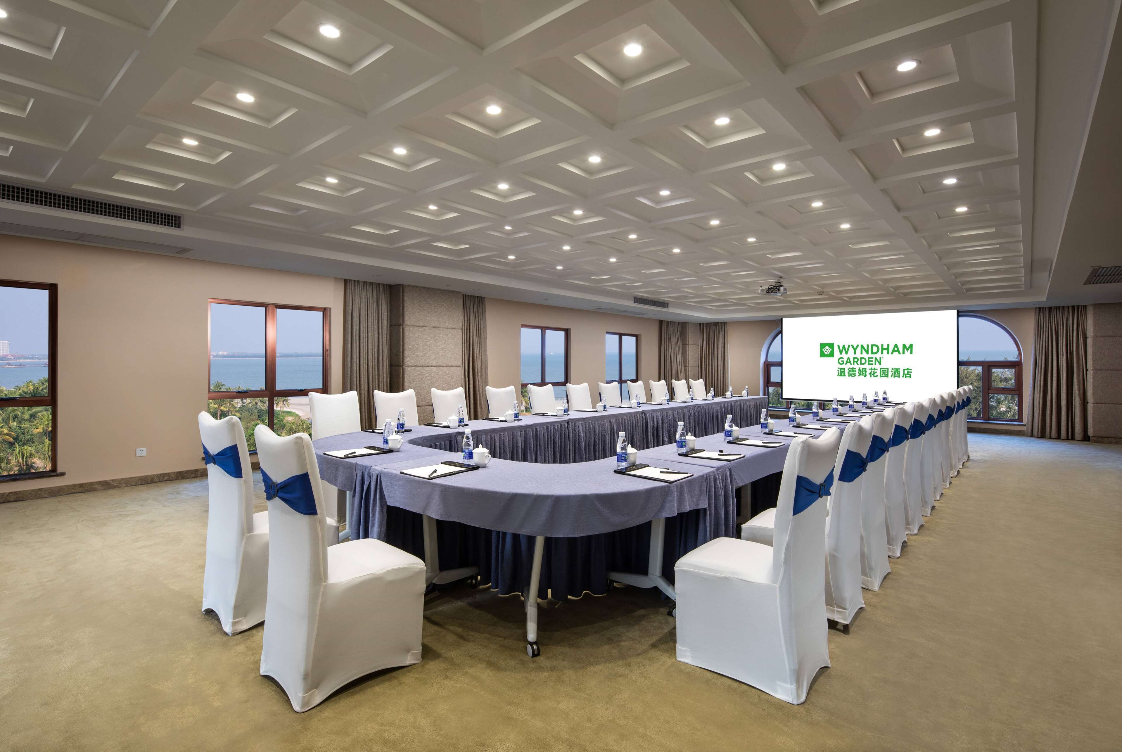 A conference room with a long table, white chairs with blue sashes, and a projector screen displaying 'WYNDHAM GARDEN'.