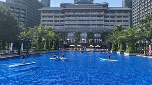 Un hôtel doté d’une grande piscine entourée de palmiers et d’un immeuble à plusieurs étages avec des balcons.