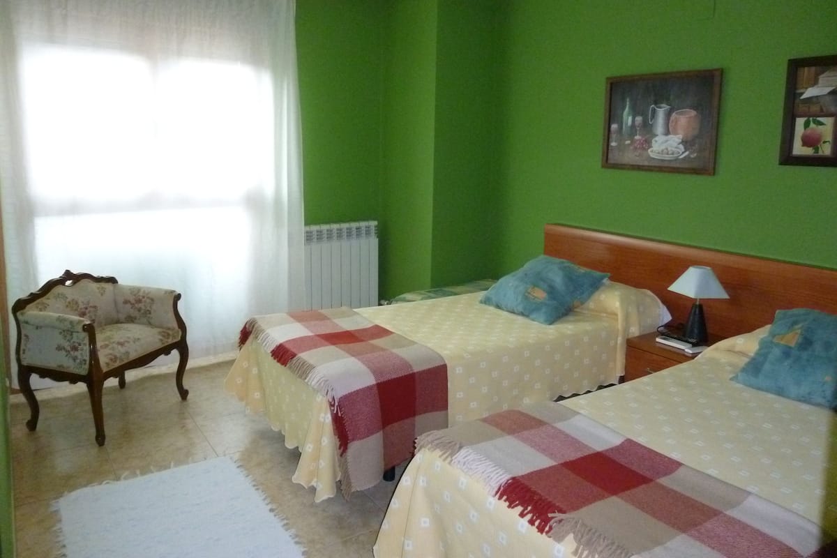 Une chambre avec deux lits, une chaise, un radiateur et une fenêtre avec des rideaux.
